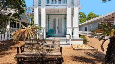 a wooden bench sitting in front of a house at Walking on Waves in Santa Rosa Beach