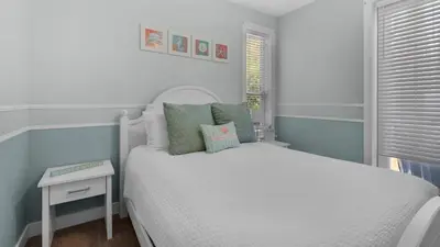 a small bedroom with a white bed and a table at Walking on Waves in Santa Rosa Beach