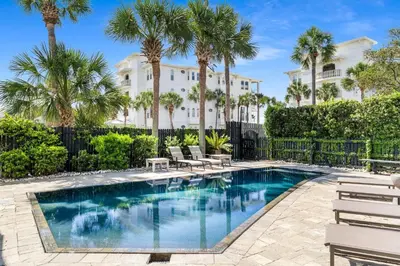 a pool with chairs and palm trees in front of a building at 99 Sandy Shores Ct in Inlet Beach
