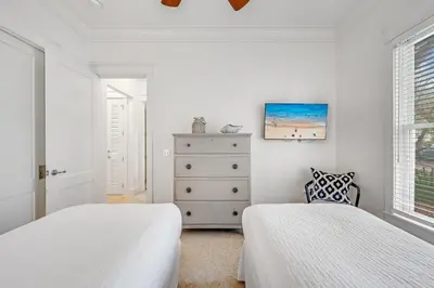 a white bedroom with two beds and a dresser at Treetop Cottage in Rosemary Beach