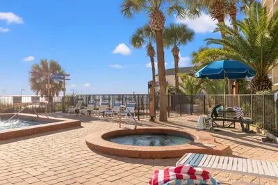 a patio with a pool and chairs and palm trees at Commodore 0502 in Panama City Beach
