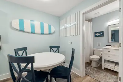 a dining room with a table and chairs and a surfboard on the wall at Blue & Red Neptune by Nautical Properties Vacation Rentals in Panama City Beach