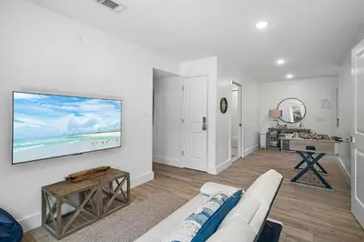 a living room with a white couch and a tv on a wall at Beach & Bubbles in Santa Rosa Beach