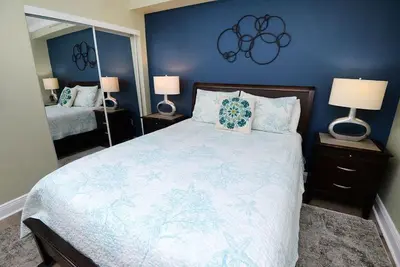 a bedroom with a large bed with blue walls and two lamps at Emerald Beach 1130 in Panama City Beach