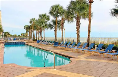a swimming pool with blue chairs and palm trees at Sterling Reef 902 in Panama City Beach