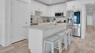 a kitchen with white cabinets and a large island with bar stools at Villas At Sunset Beach B201 in Panama City Beach