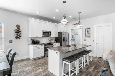 a kitchen with white cabinets and a kitchen island with bar stools at Beach House - Lazee Daze by Panhandle Getaways in Panama City Beach