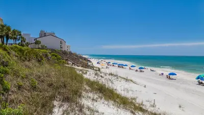 a beach with umbrellas and people sitting on the sand at Hidden Beach 201 in Santa Rosa Beach
