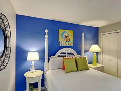 a bedroom with a white bed with a blue wall at Edgewater Tower III #113 in Panama City Beach