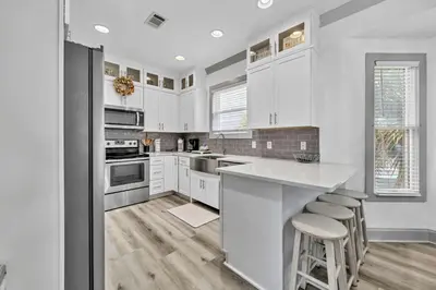 a kitchen with white cabinets and a counter with stools at Grouper Therapy in Santa Rosa Beach