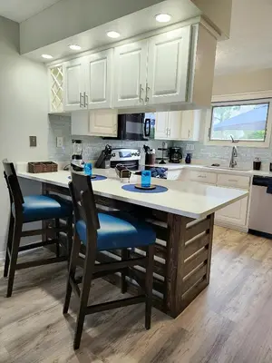 a kitchen with white cabinets and a large island with chairs at Blue By The Bay in Panama City Beach