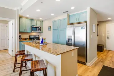 a kitchen with blue cabinets and a counter with stools at Ocean Front Condo Panama City Beach in Panama City Beach