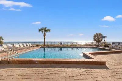 a swimming pool at the beach with chairs and the ocean at Commodore 1009 in Panama City Beach