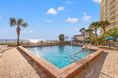 a swimming pool with palm trees and a building at Commodore 1009 in Panama City Beach