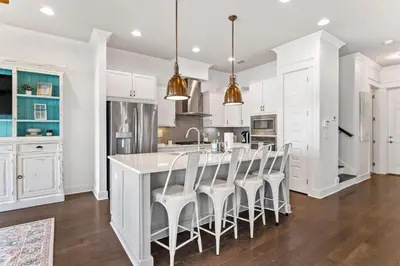 a kitchen with white cabinets and a bar with stools at Island Lullaby in Inlet Beach
