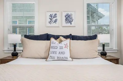 a bedroom with a bed with pillows and two windows at Lucky Beach in Inlet Beach