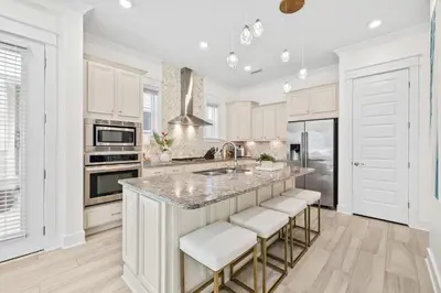 a kitchen with white cabinets and a island with bar stools at Amen 30A in Inlet Beach