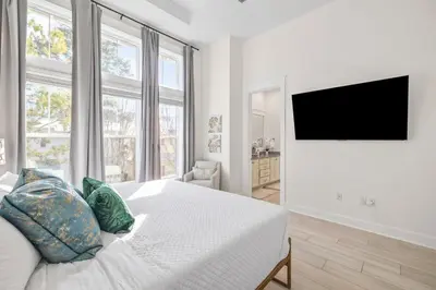 a white bedroom with a bed and a flat screen tv at Amen 30A in Inlet Beach