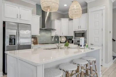 a kitchen with white cabinets and a large island with bar stools at 30Yay Home in Inlet Beach