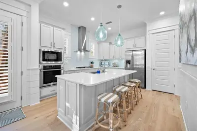 a kitchen with white cabinets and a large island with bar stools at Doc's House in Inlet Beach