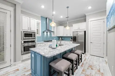 a kitchen with white cabinets and a blue island with stools at Endless Summer in Inlet Beach