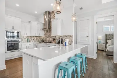 a white kitchen with white cabinets and blue stools at No Worries, Beach Happy in Inlet Beach