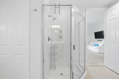 a glass shower in a white room with a television at The Alexander in Seacrest