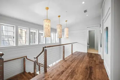 a hallway with white walls and a staircase with two chandeliers at Sadie's Cottage in Rosemary Beach