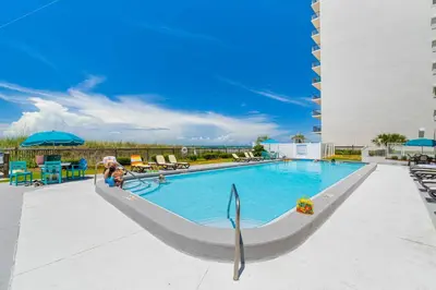 a person sitting next to a swimming pool at a hotel at Mariner West #403 in Panama City Beach