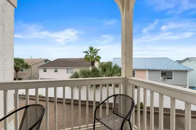 a balcony with two chairs and palm trees at Tranquil Beach & Hot Tub & Pool Getaway in Panama City Beach