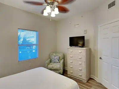a bedroom with a bed and a tv and a chair at Seychelles #206 in Panama City Beach