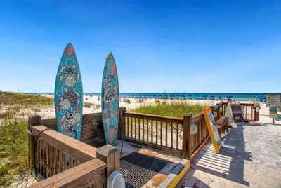 two surfboards leaning against a wooden fence at the beach at 1BR Sleeps 5 at The Summit with Ocean Front Views in Panama City Beach