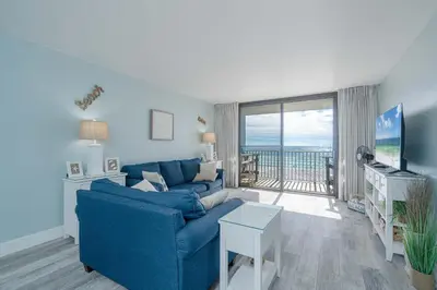 a living room with a blue couch and a balcony at Edgewater Oasis Gorgeous Resort Condo on Beach in Panama City Beach