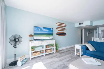a living room with a blue couch and a tv at Edgewater Oasis Gorgeous Resort Condo on Beach in Panama City Beach