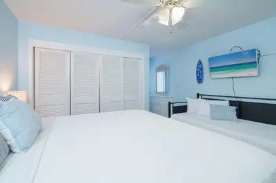 a bedroom with two white beds and a blue wall at Sea Forever - Cozy Oceanfront Condo in Panama City Beach