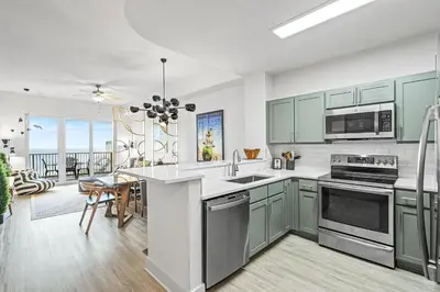 a kitchen with green cabinets and a dining room at Salt and Shore Escape - Sleeps 7 in Panama City Beach