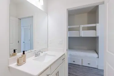 a white bathroom with a sink and a bunk bed at Sandy Feet Retreat - Ocean View Condo in Panama City Beach