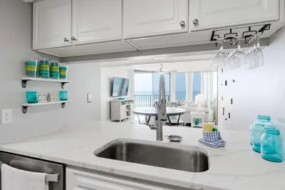 a white kitchen with a sink and a table at Beachfront Days Ocean View Condo Bliss in Panama City Beach