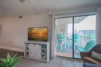 a living room with a flat screen tv and a balcony at Bethys Beachy Beauty Regency Towers in Panama City Beach