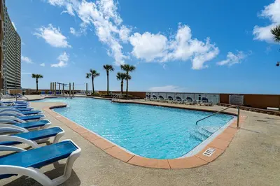 a large swimming pool with chairs and palm trees at Sunrise Sands - An Unforgettable Vacation for 7 in Panama City Beach