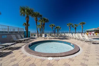 a pool with chairs and palm trees on a beach at Sunrise Sunset - Full Ocean Views in Panama City Beach