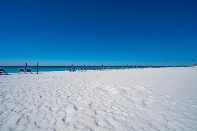 a white sandy beach with chairs and a pier at Sunrise Sunset - Full Ocean Views in Panama City Beach