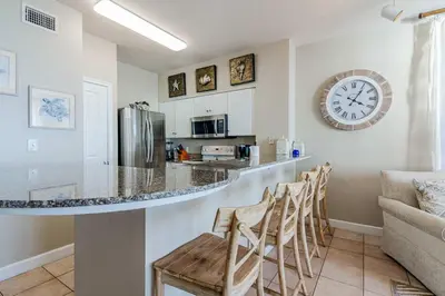 a kitchen with a bar with chairs and a clock on the wall at Sunset Shores - Oceanfront Condo Bliss in Panama City Beach