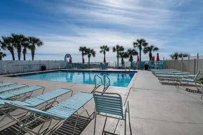 a swimming pool with blue chairs and palm trees at The Turtle Nest - Resort Condo with Pool in Panama City Beach