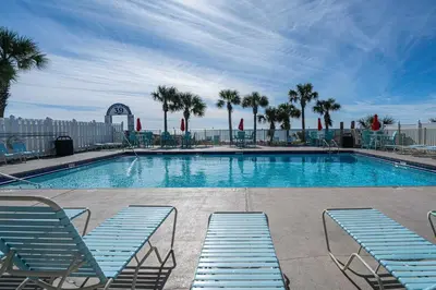a large swimming pool with blue chairs and palm trees at The Turtle Nest - Resort Condo with Pool in Panama City Beach