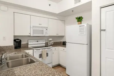 a white kitchen with a sink and a refrigerator at Shores of Panama Beachfront 2nd Floor Unit 208! No elevators needed! in Panama City Beach