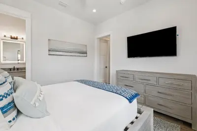 a white bedroom with a bed and a flat screen tv at White Sand Retreat by 30A Escapes in Seagrove Beach
