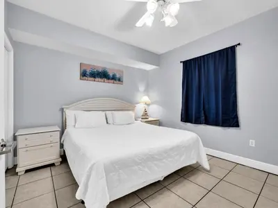 a bedroom with a white bed and a blue curtain at Celadon 203 in Panama City Beach