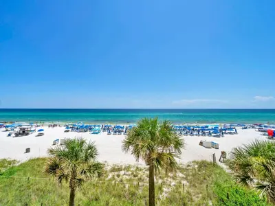 a beach with palm trees and blue umbrellas and the ocean at Celadon 203 in Panama City Beach