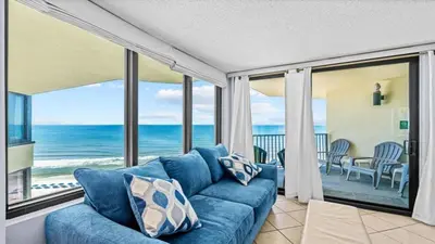 a living room with a blue couch and a view of the ocean at Sunbird Resort - 11th Floor - Free Beach Chairs - by Sunbird Rentals in Panama City Beach